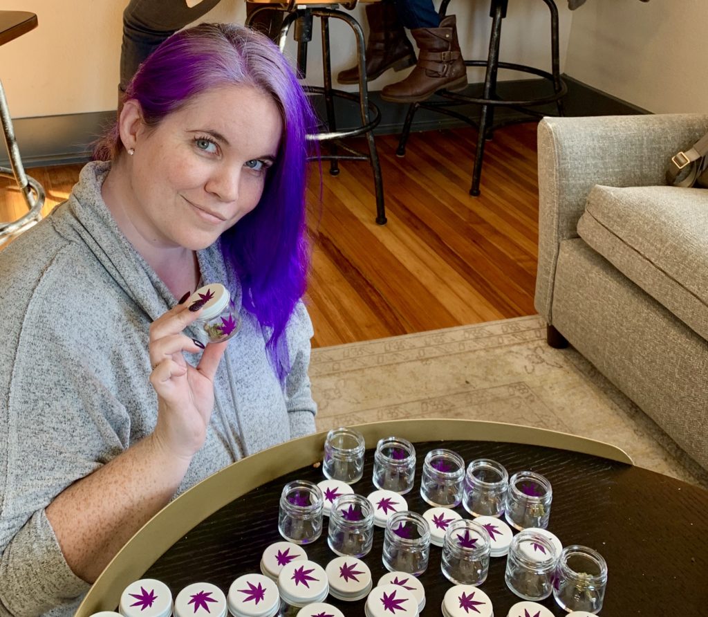 Woman with purple hair holds class jar with purple cannabis sticker. 